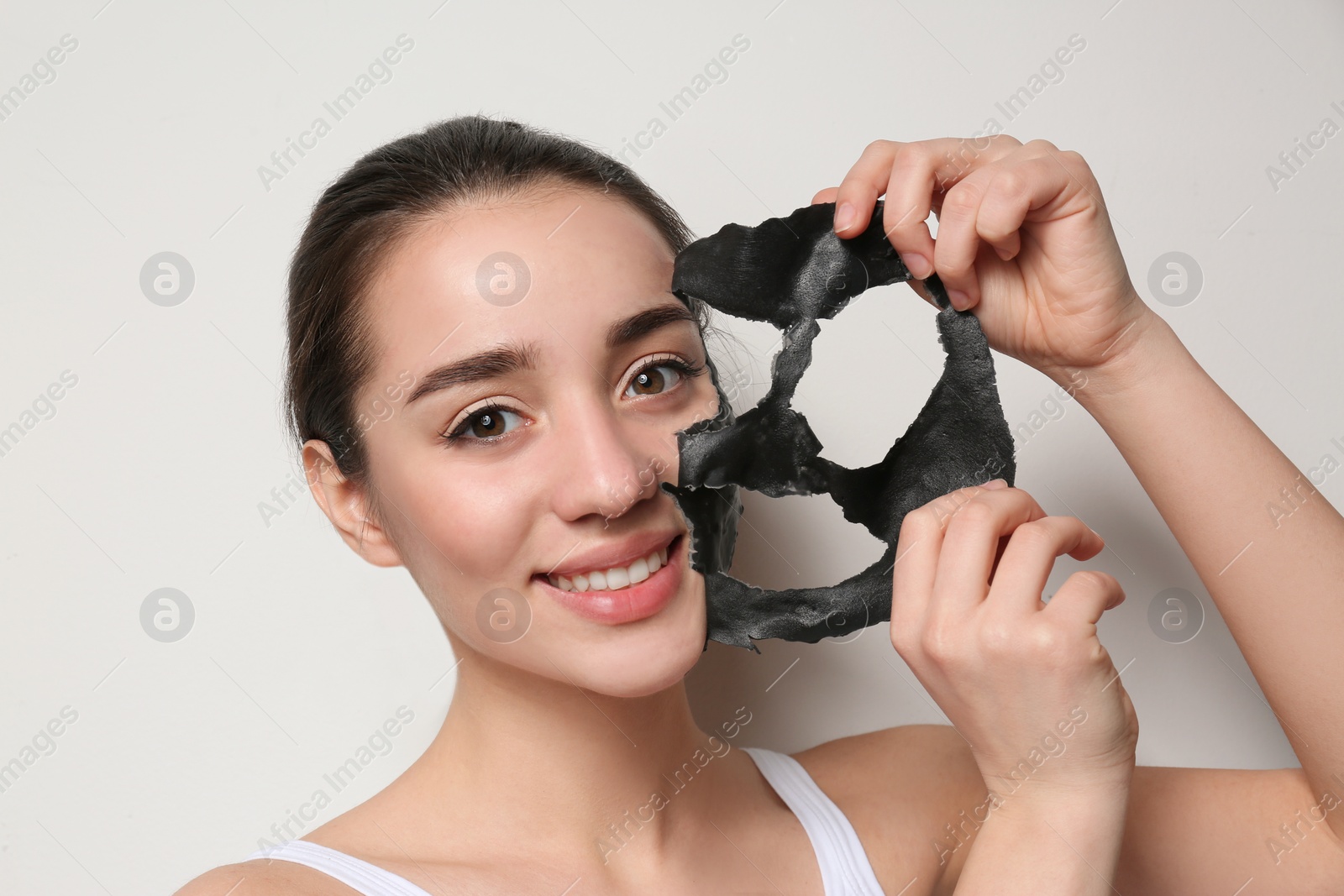 Photo of Beautiful young woman removing black mask from her face on white background