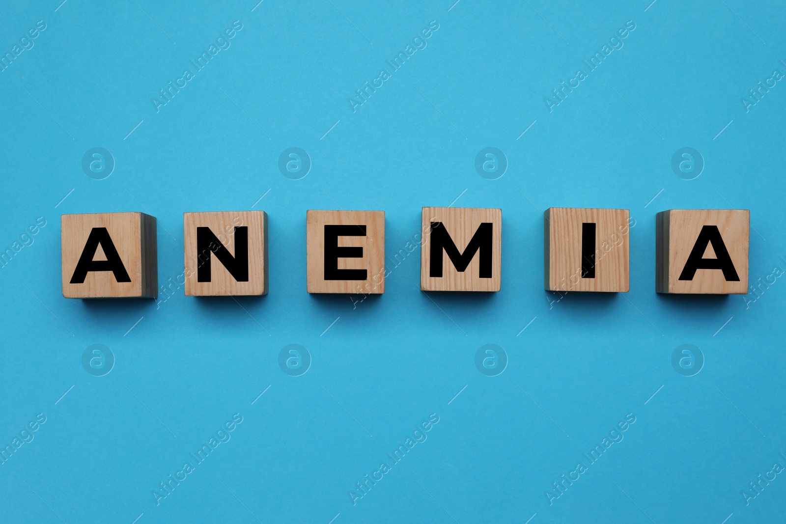 Photo of Wooden cubes with word Anemia on light blue background, flat lay