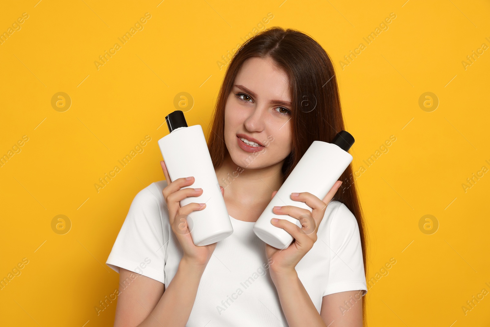 Photo of Beautiful young woman holding bottles of shampoo on yellow background
