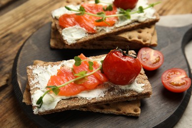 Photo of Fresh rye crispbreads with salmon, cream cheese and tomatoes on wooden table, closeup