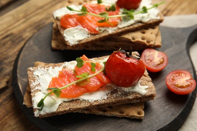 Fresh rye crispbreads with salmon, cream cheese and tomatoes on wooden table, closeup