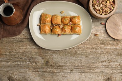 Photo of Delicious baklava with pistachios and hot coffee on wooden table, flat lay. Space for text