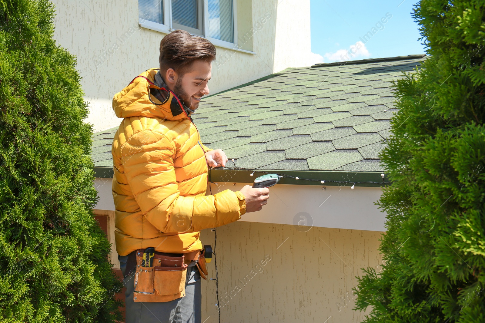 Photo of Young man decorating roof with Christmas lights