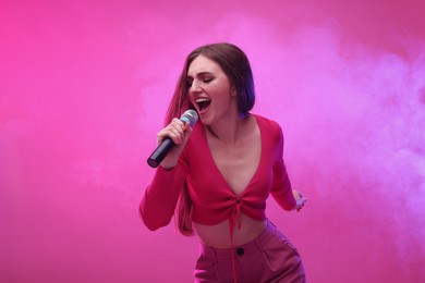 Emotional woman with microphone singing on pink background