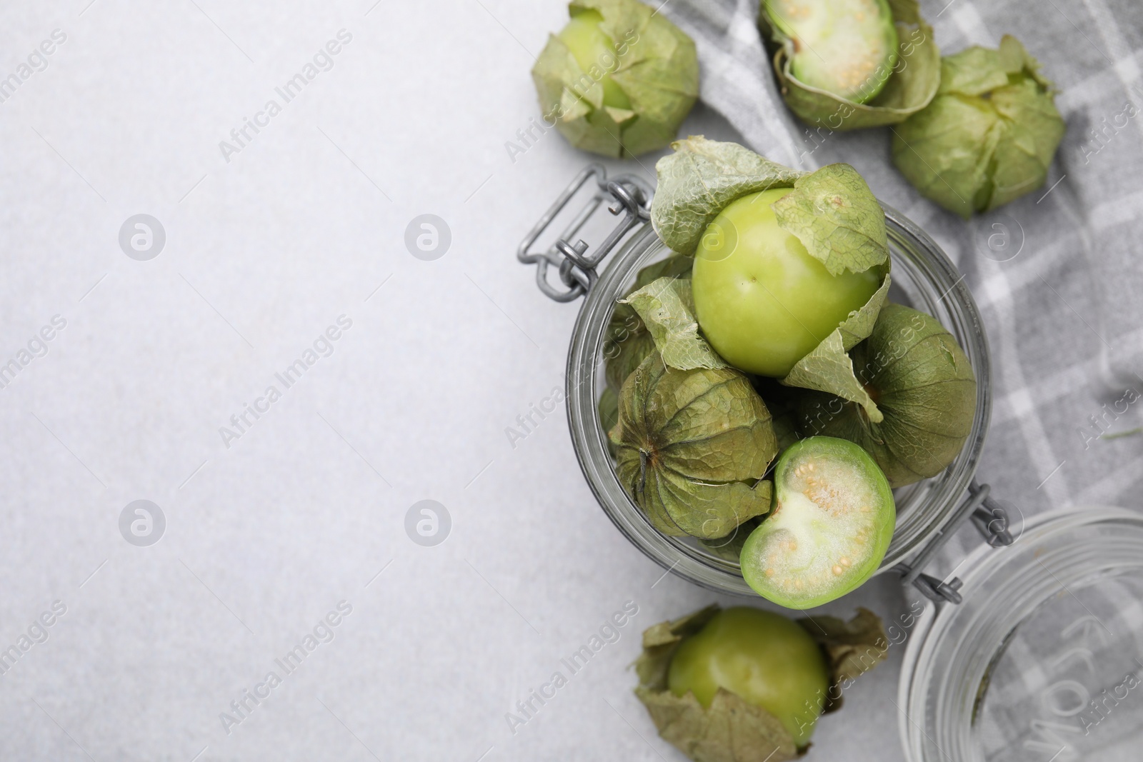 Photo of Fresh green tomatillos with husk in glass jar on light table, flat lay. Space for text