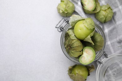 Fresh green tomatillos with husk in glass jar on light table, flat lay. Space for text