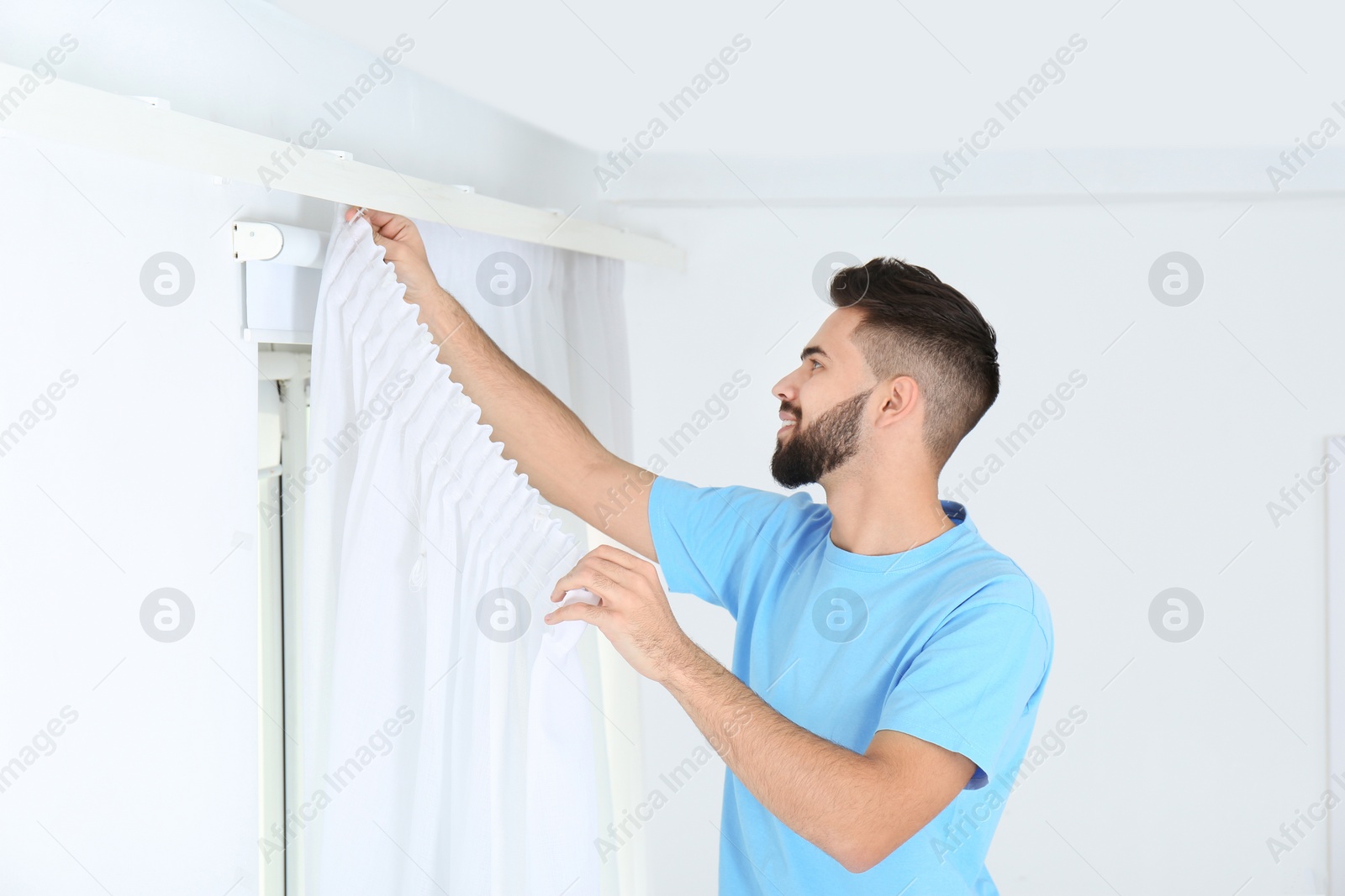 Photo of Young handsome man hanging window curtain in room
