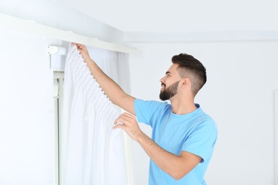 Young handsome man hanging window curtain in room