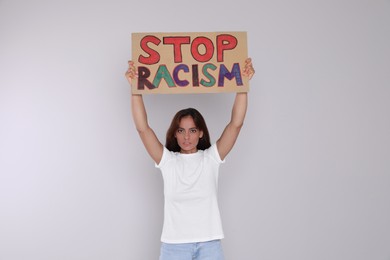 Photo of Young woman holding sign with phrase Stop Racism on light background
