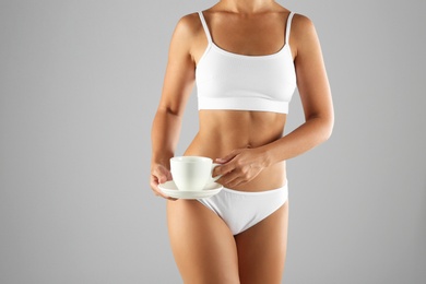 Photo of Young woman holding cup of diet tea on grey background, closeup