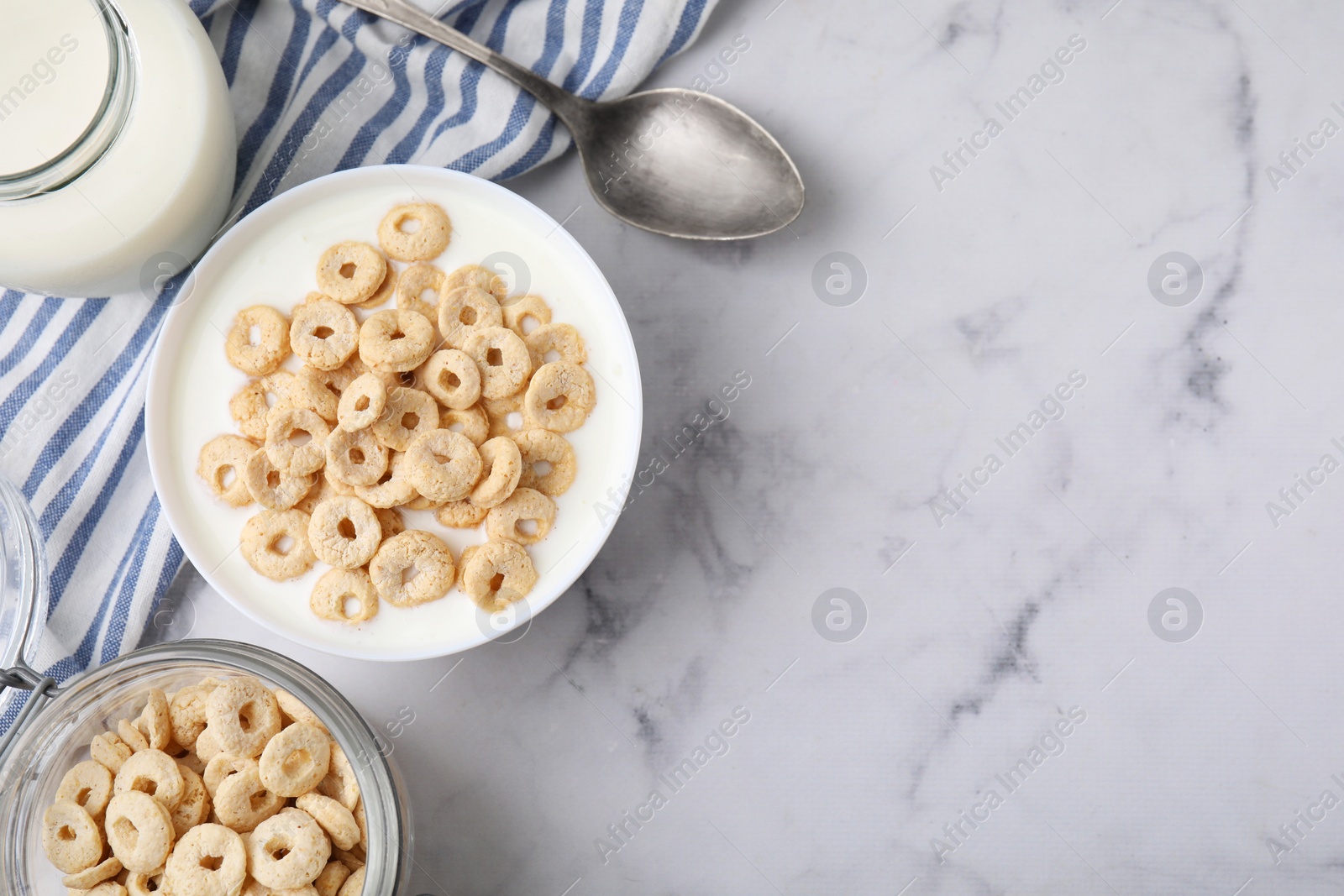 Photo of Breakfast cereal. Tasty corn rings, milk and spoon on white marble table, top view. Space for text