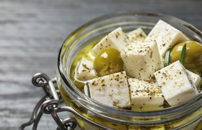 Photo of Pickled feta cheese in jar on grey wooden table, closeup