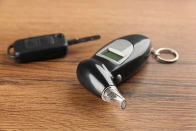 Modern breathalyzer and car key on wooden table