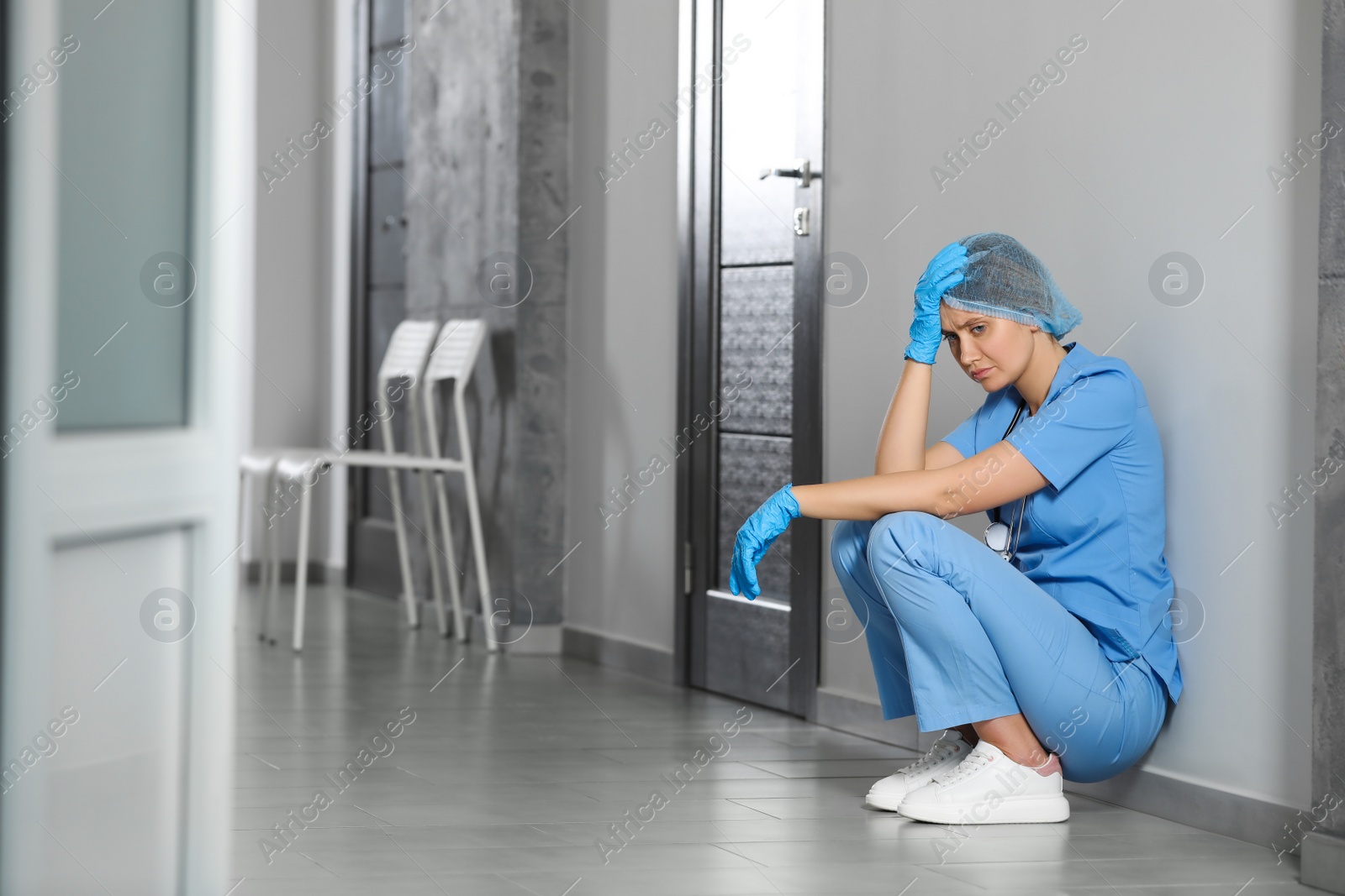 Photo of Exhausted doctor sitting on floor in hospital, space for text