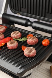 Photo of Electric grill with vegetables and meat balls on table, closeup