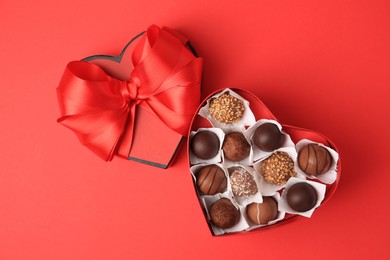 Photo of Heart shaped box with delicious chocolate candies on red table, flat lay