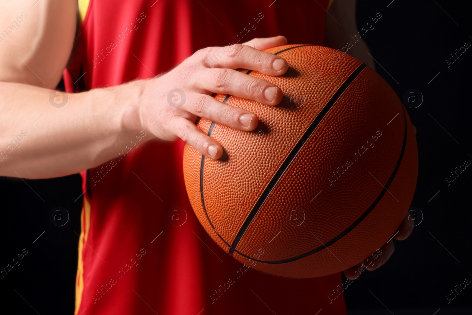 Photo of Athletic man with basketball ball on black background, closeup