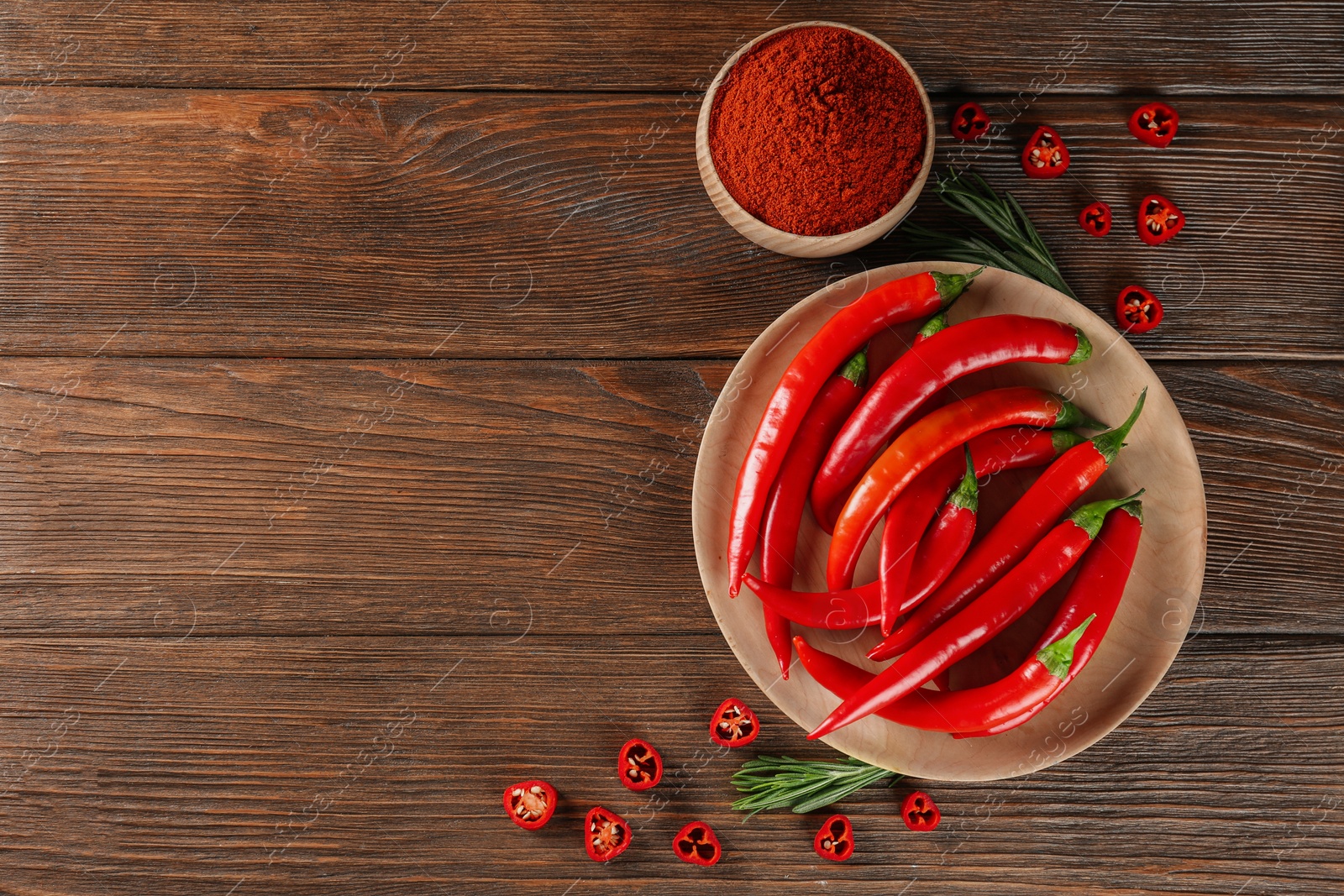 Photo of Bowl of ground red pepper with ingredients on wooden table, flat lay. Space for text