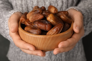 Photo of Woman holding bowl with tasty dried date fruits, closeup