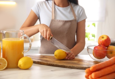 Photo of Young woman cutting fresh lemon for juice at table in kitchen, closeup