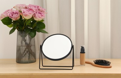 Photo of Mirror, foundation, brush and vase with pink roses on wooden dressing table