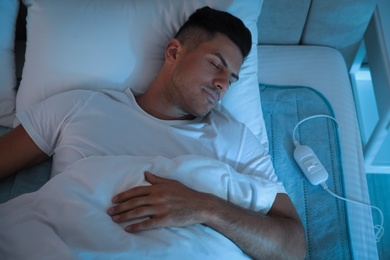 Photo of Man sleeping on electric heating pad in bed at night, above view