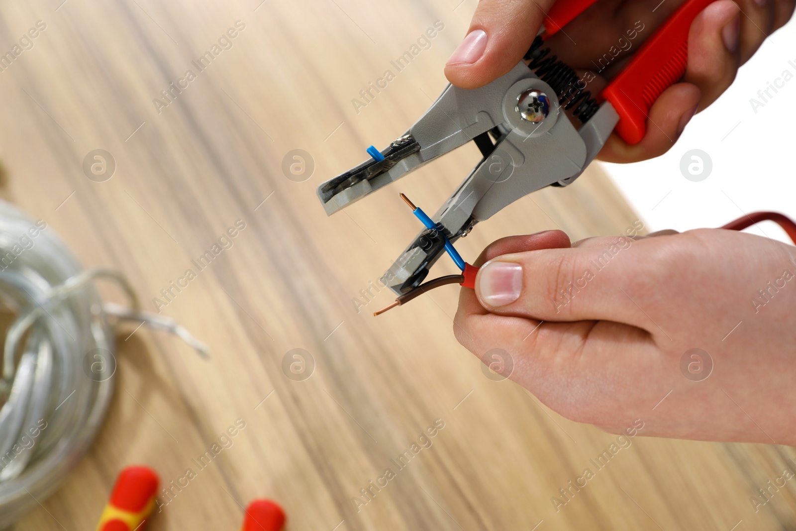 Photo of Professional electrician stripping wiring at wooden table, top view