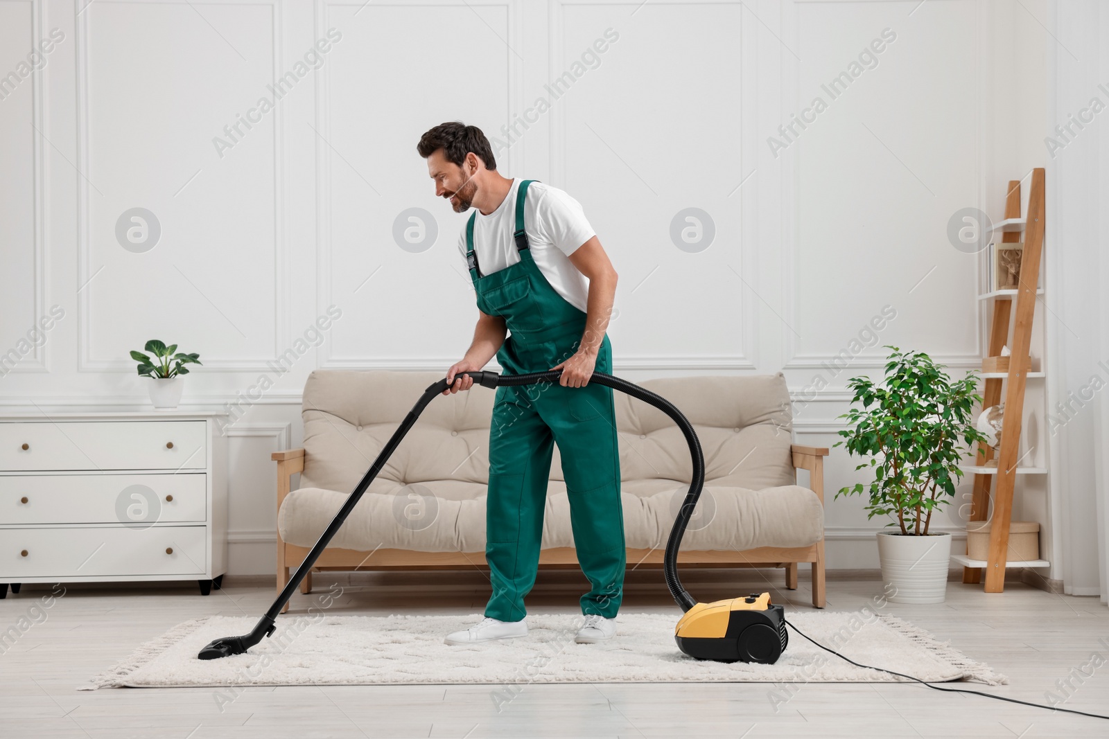 Photo of Dry cleaner's employee hoovering carpet with vacuum cleaner in room