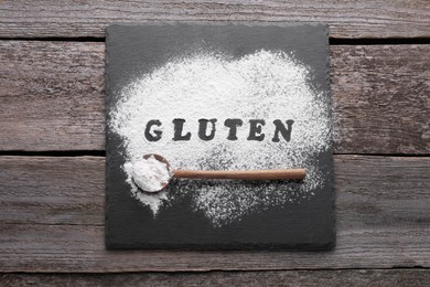 Photo of Spoon, board and word Gluten written with flour on wooden table, flat lay