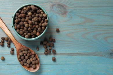 Photo of Aromatic allspice pepper grains in bowl and spoon on light blue wooden table, flat lay. Space for text