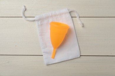 Photo of Menstrual cup with cotton bag on white wooden background, top view