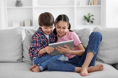 Photo of Happy brother and sister with tablet on sofa at home