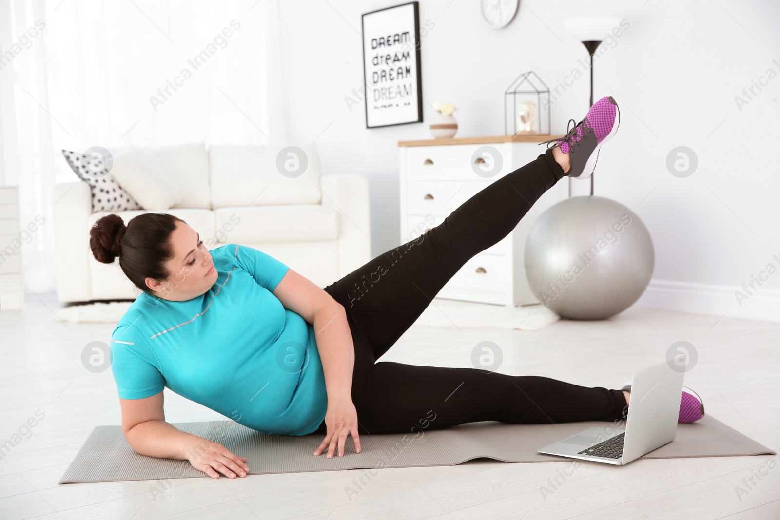 Photo of Overweight woman doing exercise while watching tutorial on laptop at home