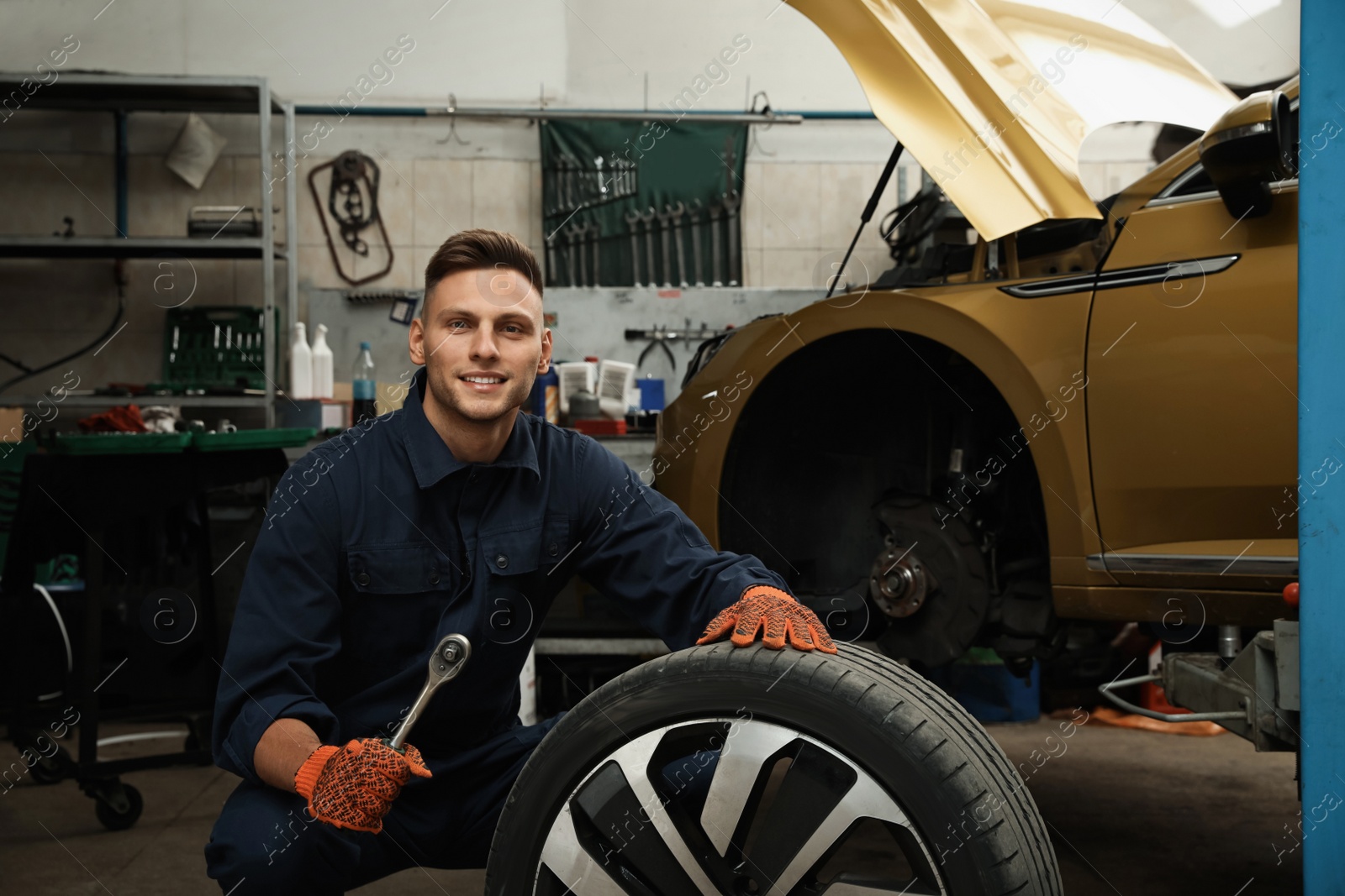 Photo of Portrait of professional mechanic with car wheel at automobile repair shop