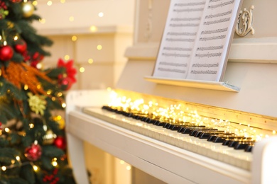 Photo of White piano with festive decor and note sheets indoors. Christmas music