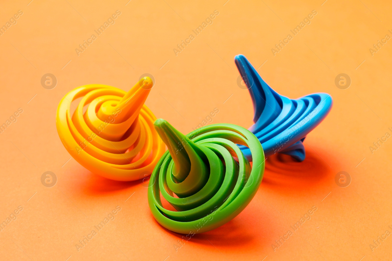 Photo of Many colorful spinning tops on orange background, closeup