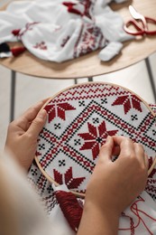 Photo of Woman embroidering white shirt with colorful threads in hoop, closeup. Ukrainian national clothes