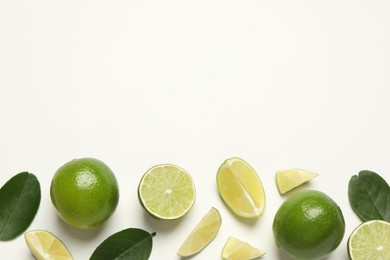 Whole and cut fresh ripe limes with green leaves on white background, flat lay