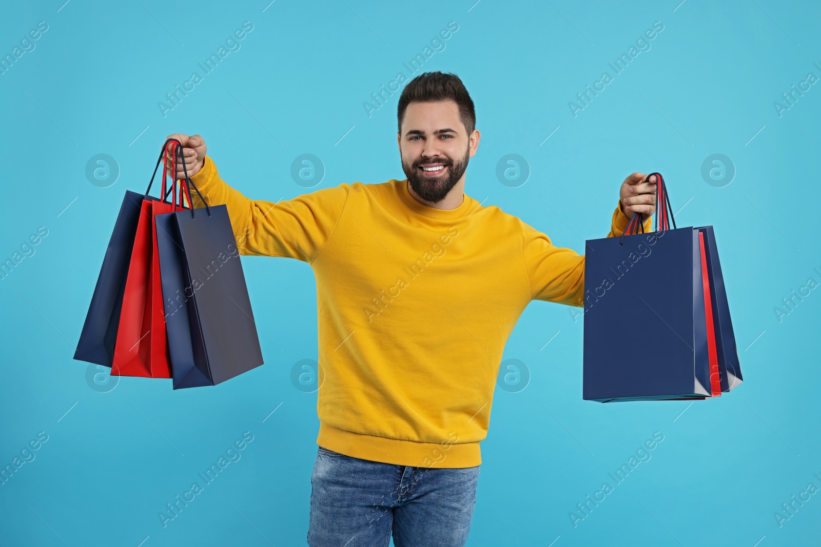 Photo of Smiling man with many paper shopping bags on light blue background