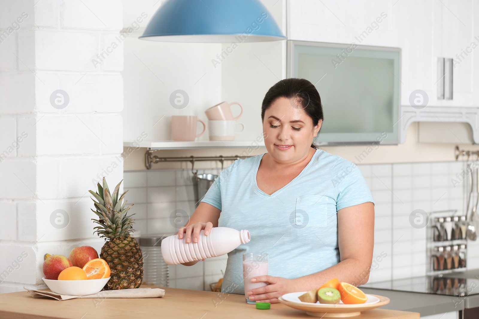 Photo of Woman pouring yogurt from bottle into glass in kitchen. Healthy diet