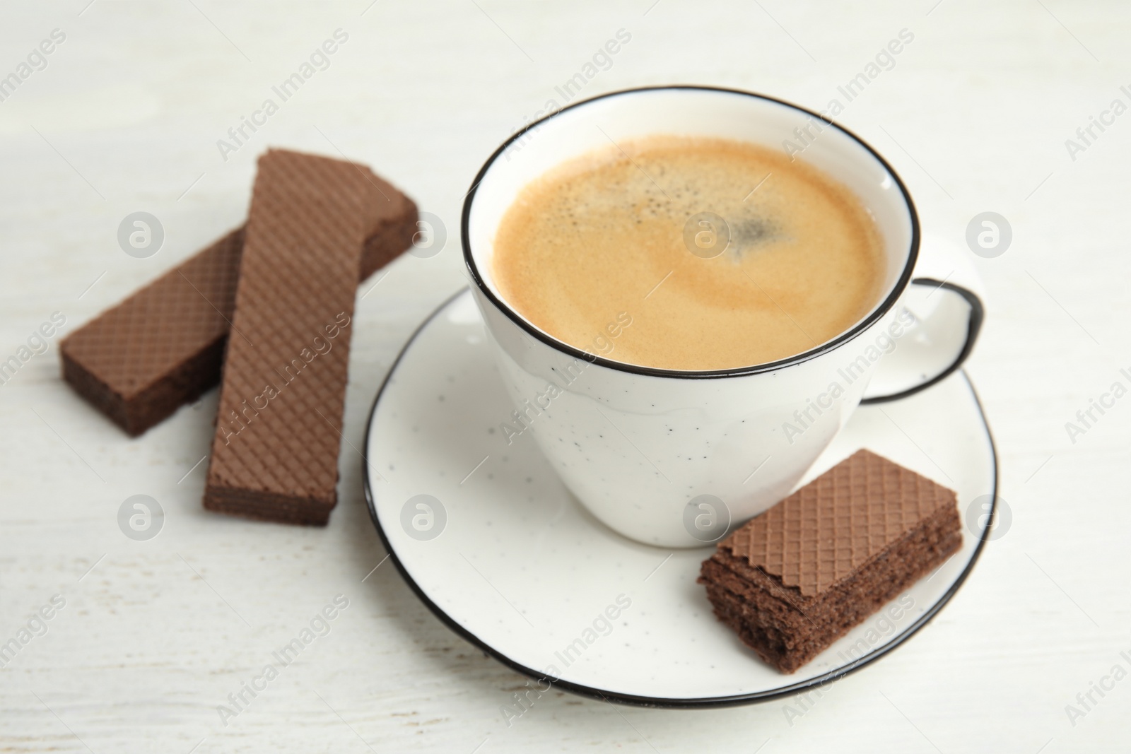 Photo of Delicious wafers and cup of coffee for breakfast on white wooden table