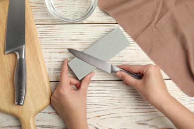 Photo of Woman sharpening knife at white wooden table, top view