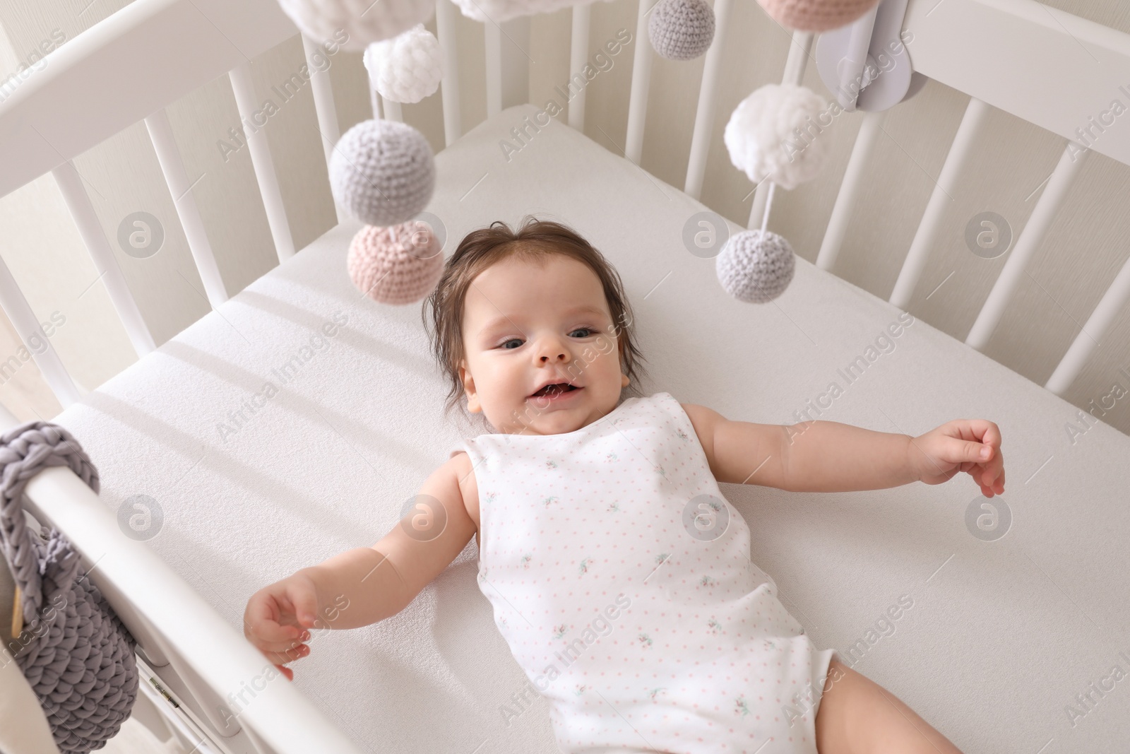 Photo of Cute little baby lying in crib with hanging mobile