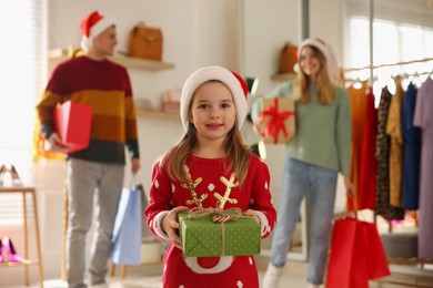 Photo of Little girl with gift box near her parents in store. Family Christmas shopping