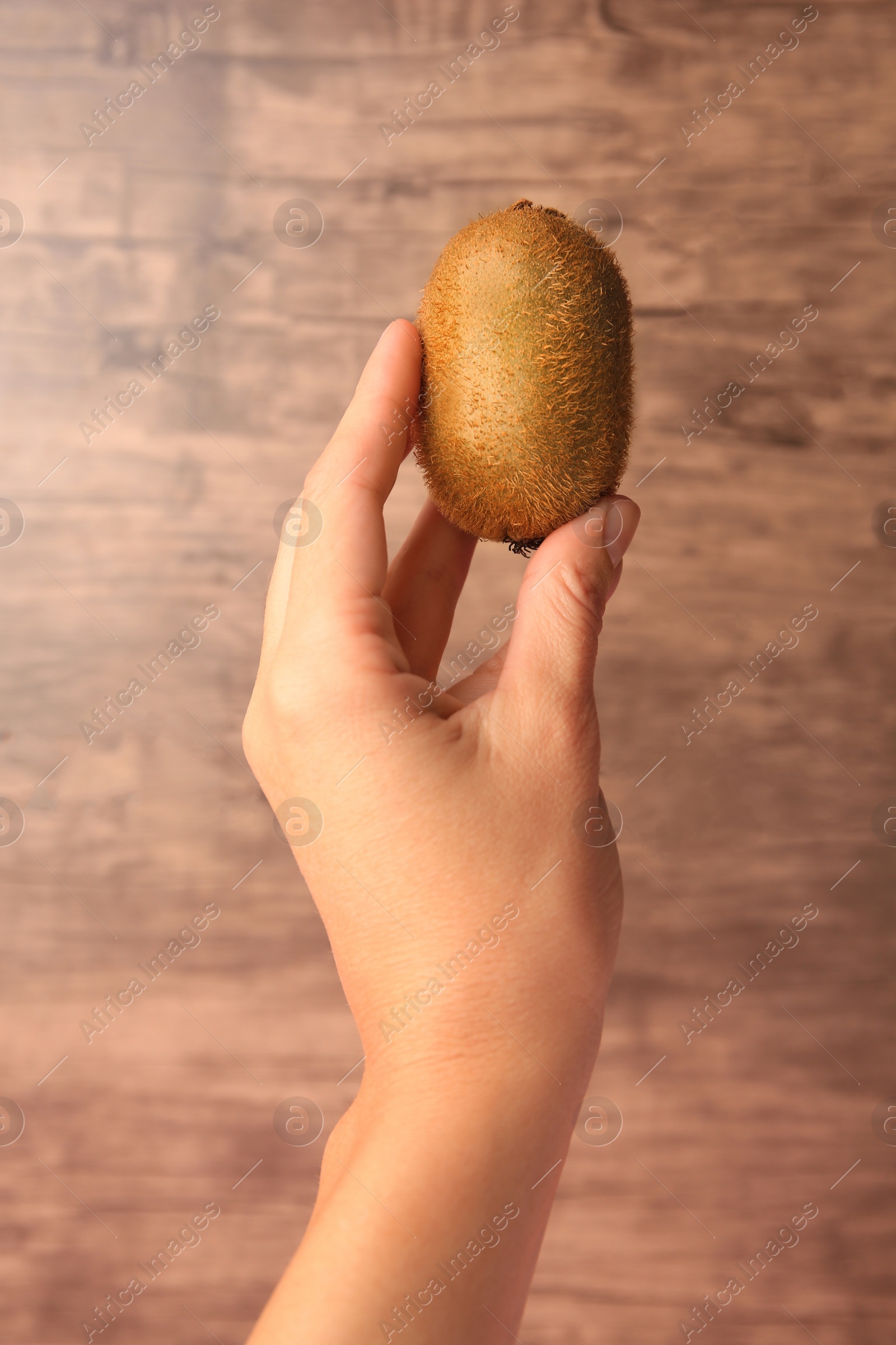 Photo of Woman holding delicious fresh kiwi on wooden background, closeup