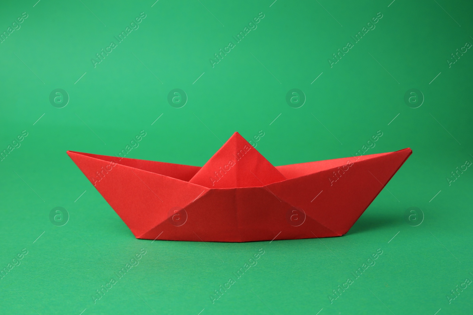 Photo of Origami art. Red paper boat on green background