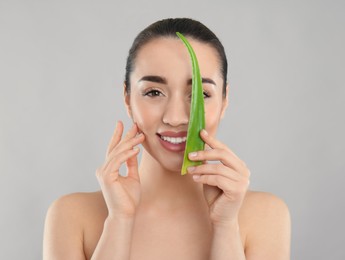 Photo of Young woman with aloe vera leaf on light grey background