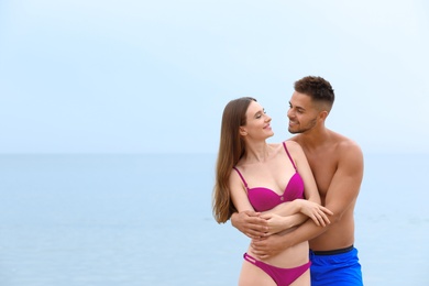 Young woman in bikini with her boyfriend on beach, space for text. Lovely couple