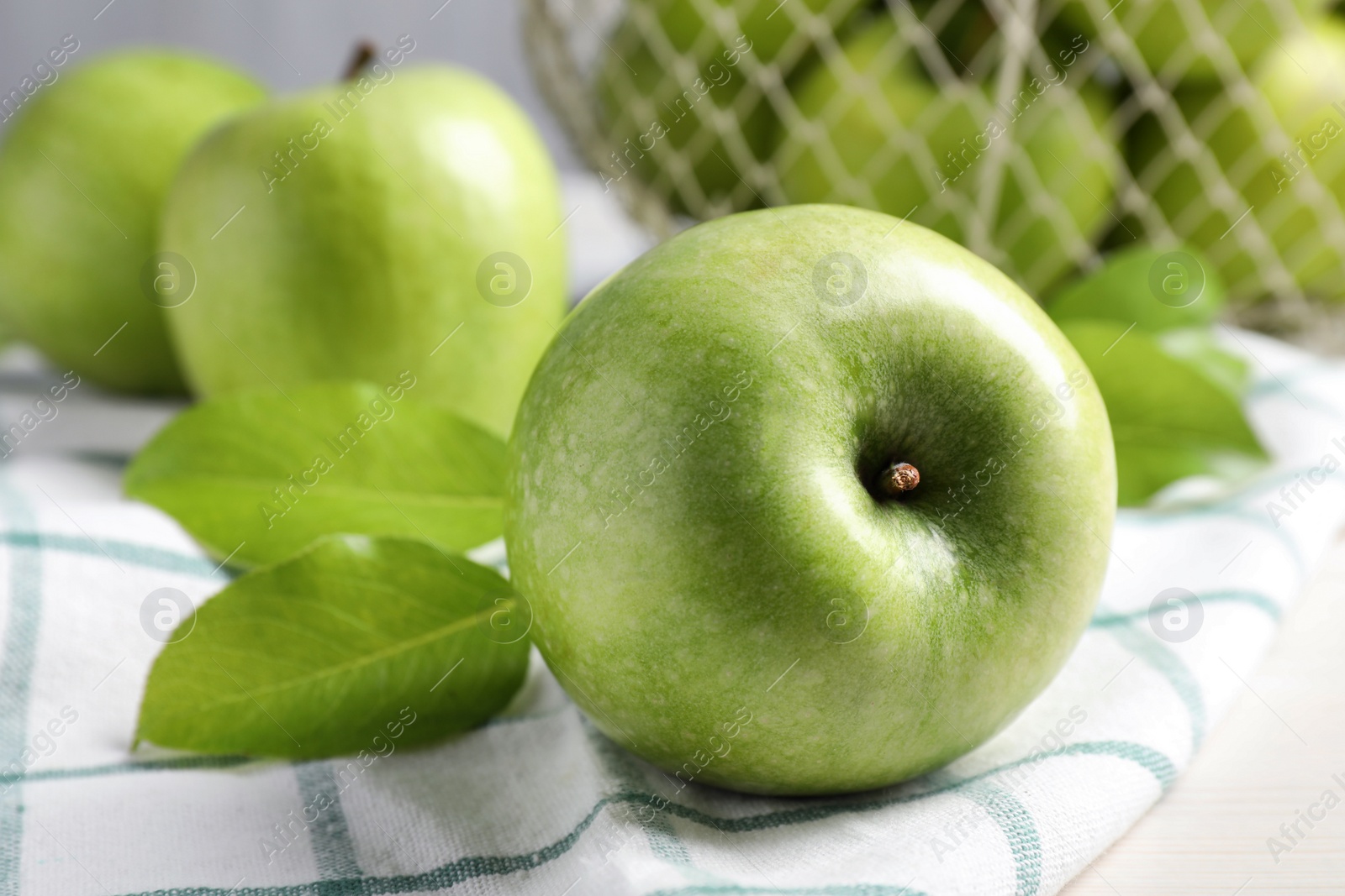 Photo of Fresh ripe green apples with leaves and napkin on table, closeup