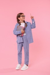 Photo of Smiling schoolgirl with books pointing at something on pink background